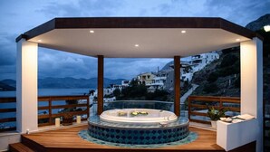A hot tub with a wooden deck and a view of a hillside town.