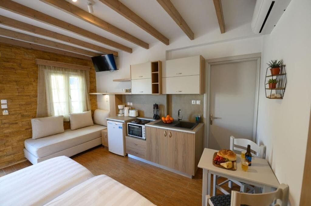 Habitación compacta con kitchenette, sofá, mesa de comedor y televisor montado en la pared.