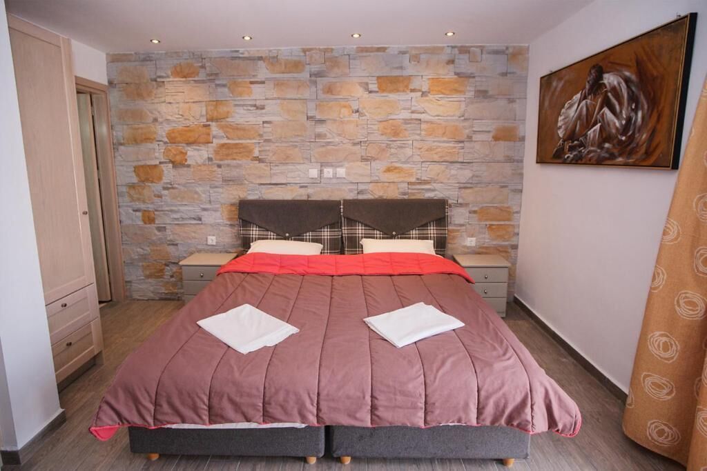 A bedroom with a stone wall, a bed with a plaid headboard, two bedside tables, and a painting on the wall.