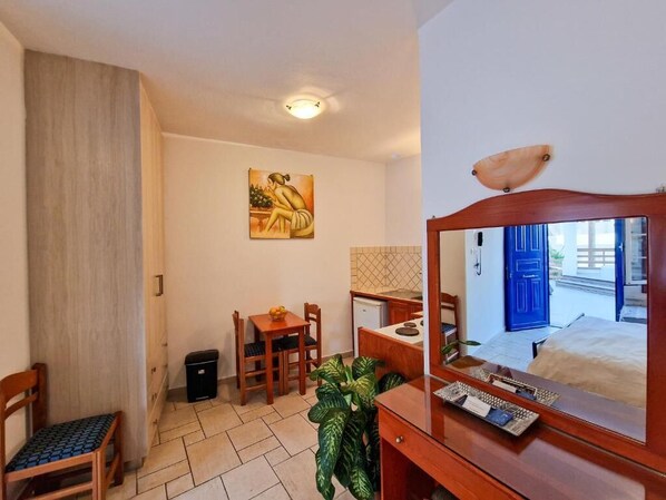 Una habitación de hotel con una cama, un escritorio, una silla, una mesita con una planta, un espejo y un cuadro en la pared.