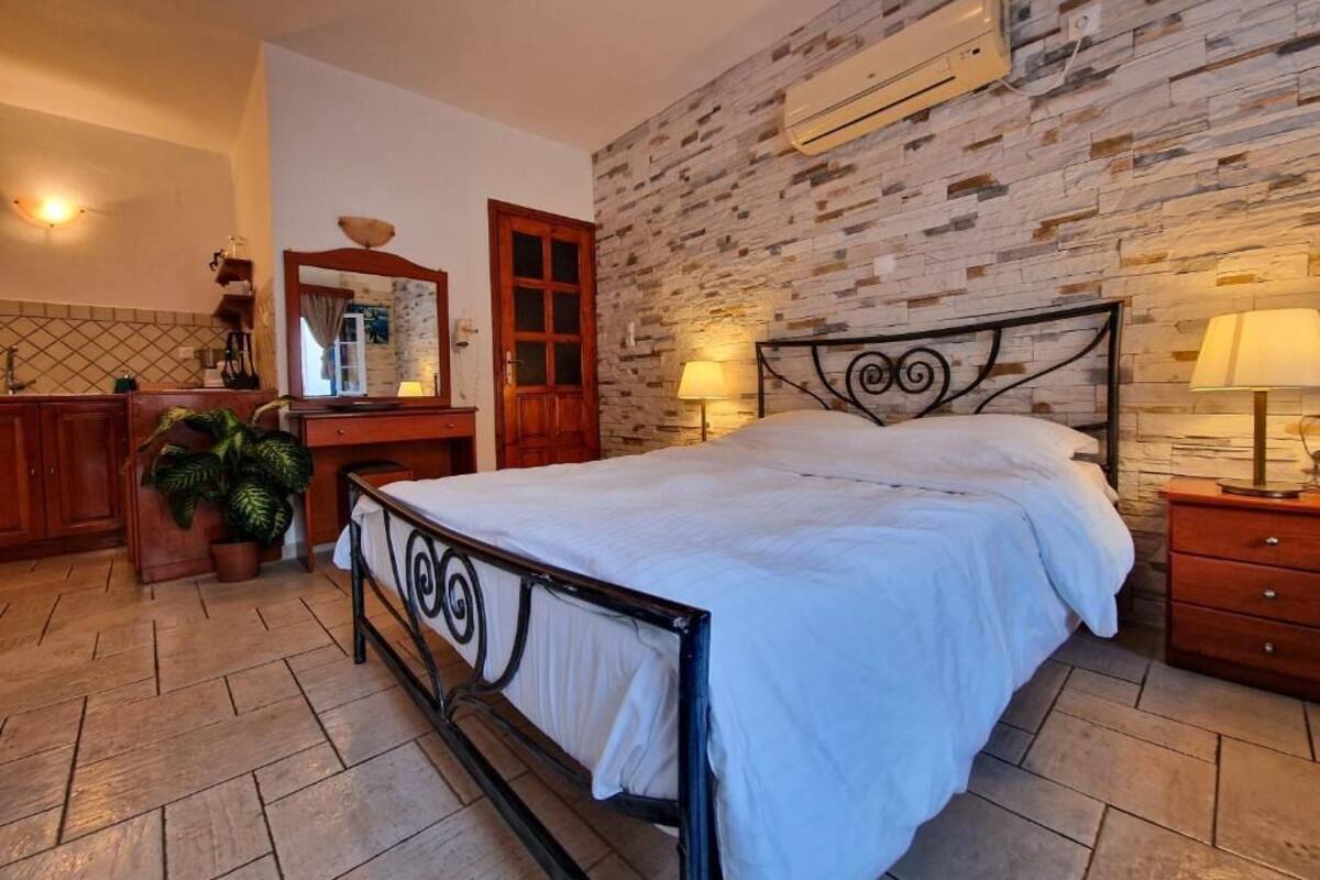 A bedroom with a bed, a dresser, a mirror, a potted plant, and a stone wall.