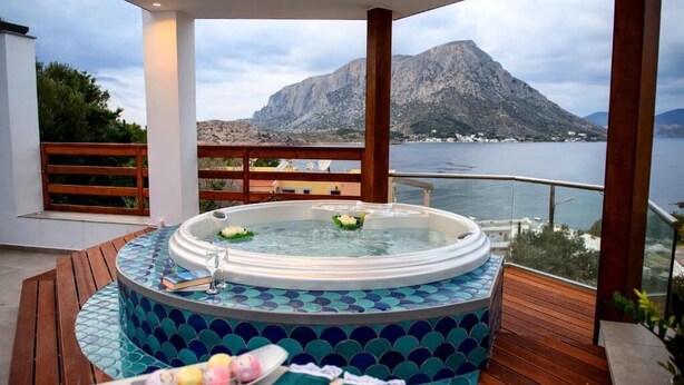 A hot tub on a wooden deck with a view of a mountain and water.