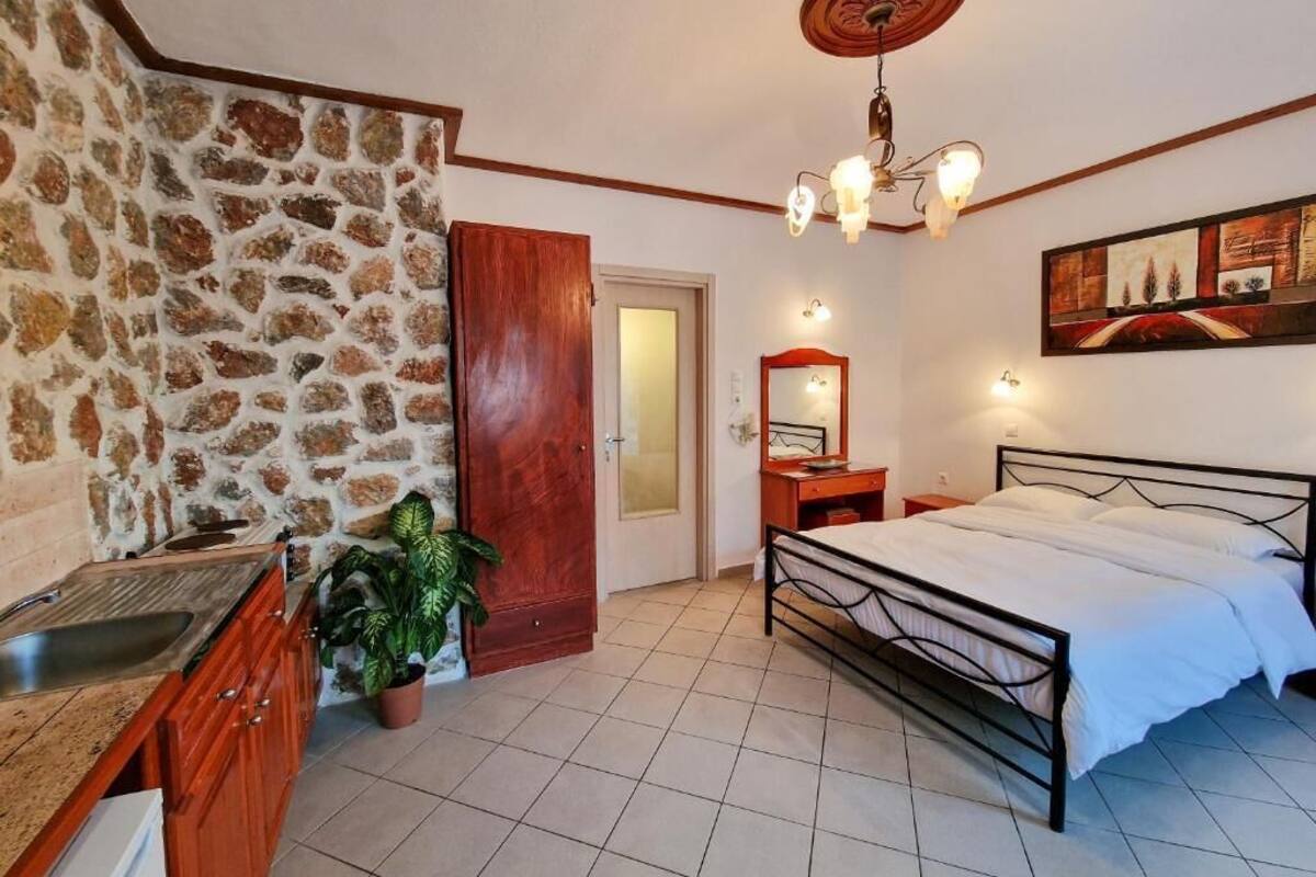 A bedroom with a stone wall, a bed, a wooden dresser, a potted plant, a mirror, and a chandelier.