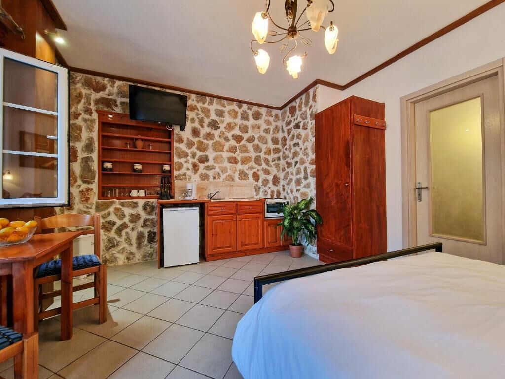 A bedroom with a bed, a small kitchenette, a dining area with a table and chairs, and a stone wall.