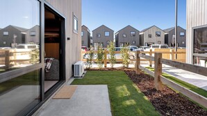 Un edificio moderno con amplios ventanales, una terraza de madera y un pequeño jardín.