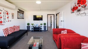 Ein Wohnzimmer mit einem schwarzen Sofa, einem roten Sofa, einem Glastisch und einem Fernseher an der Wand.