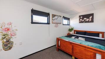 A bedroom with a wooden bed, a window, a wall-mounted picture, and a vase with flowers.