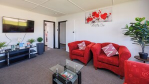 Ein Wohnzimmer mit Flachbildfernseher, roten Sofas, einem Glastisch und einem Blumentopf.