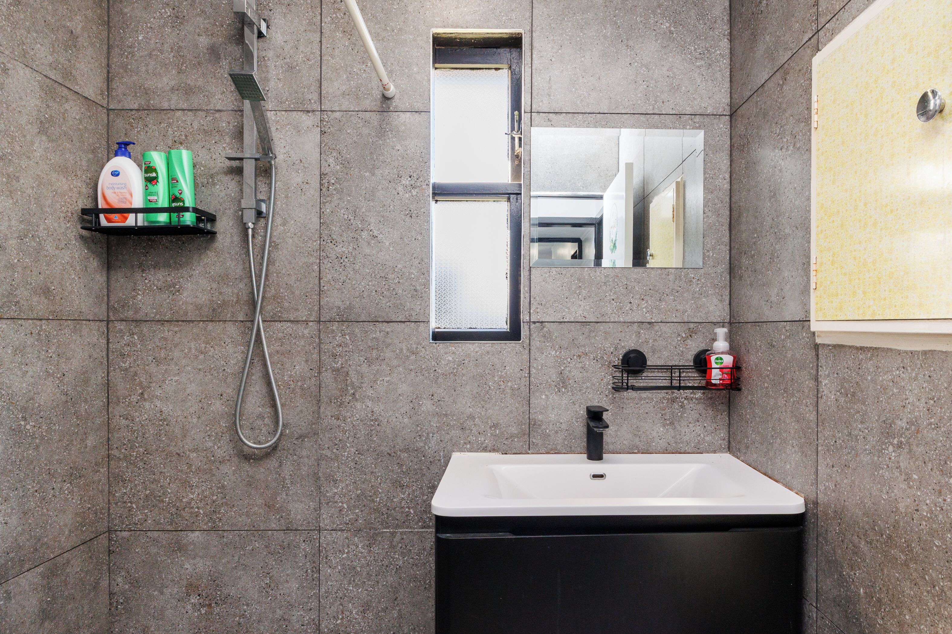 Une salle de bain équipée d’une douche, d’un lavabo, d’un miroir et de produits de toilette rangés sur des étagères.
