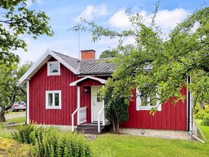 A red wooden house with a white door, a small porch, and a chimney.