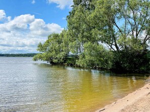 A calm lake with trees on the right and a sandy shore on the left. - 4 Person Holiday Home in Enkoping (Enkoping)