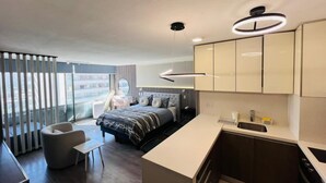 A modern hotel room with a bed, a sitting area, a kitchenette, and a large window offering a view. - Dummy Malaga (Santiago)