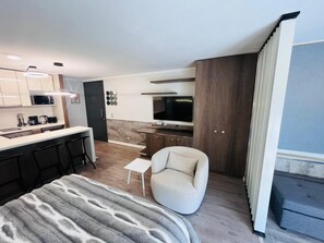 Ein modernes Hotelzimmer mit Küchenzeile, einer Couch, einem kleinen Tisch und einem Fernseher.