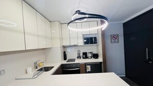 A modern kitchen with white cabinets, a black countertop, a built-in oven, and a coffee maker. - Dummy Malaga (Santiago)