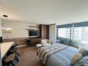 Ein modernes Hotelzimmer mit Bett, Schreibtisch, Stuhl, Fernseher und einem Balkon mit Blick.