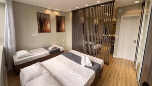 Habitación de hotel con dos camas, una puerta corrediza y un pequeño rincón de descanso.