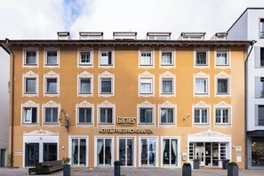 Fachada de hotel con múltiples ventanas, una entrada central y un cartel que dice 'Garner Hotel Friedrichshafen'.