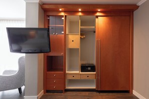 A walk-in closet with a television mounted on the wall, wooden cabinetry, and a microwave on the countertop. - Garner Hotel Friedrichshafen By IHG (Friedrichshafen)