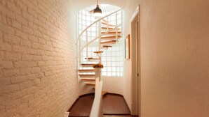 A spiral staircase with wooden steps and white railings, leading to a landing with a window and a door.