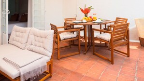 A patio with a wooden table set for breakfast, a cushioned sofa, and a wooden chair.