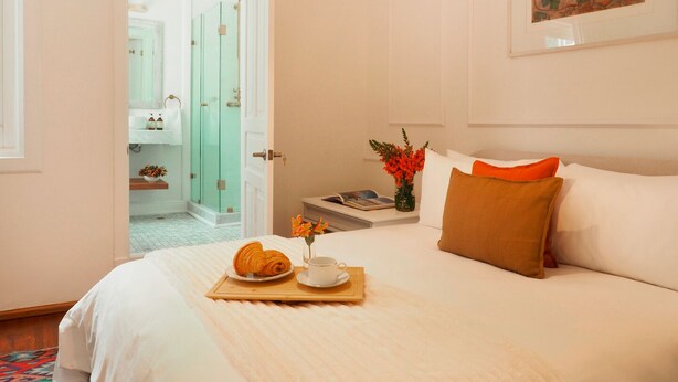 A hotel room with a bed, a tray with croissants, a vase with flowers, and a painting on the wall.