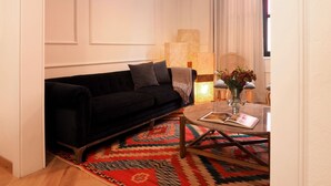 A living room with a black sofa, a patterned rug, a round coffee table with a book, and a vase with flowers.