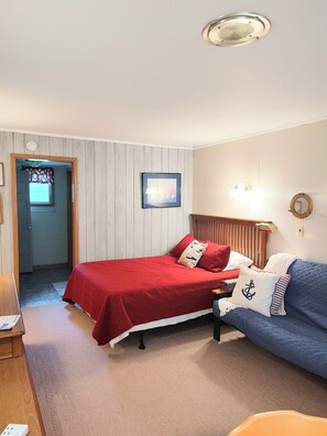 Une chambre à coucher comprenant un lit, un canapé, une table de chevet, une lampe, un tableau encadré et une porte donnant sur une autre pièce.