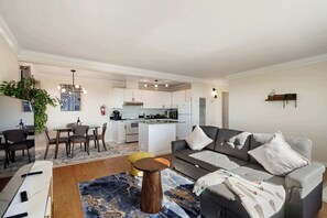 Uma sala de estar moderna com um sofá cinzento, uma mesa de centro e uma área de jantar com cadeiras e uma mesa.