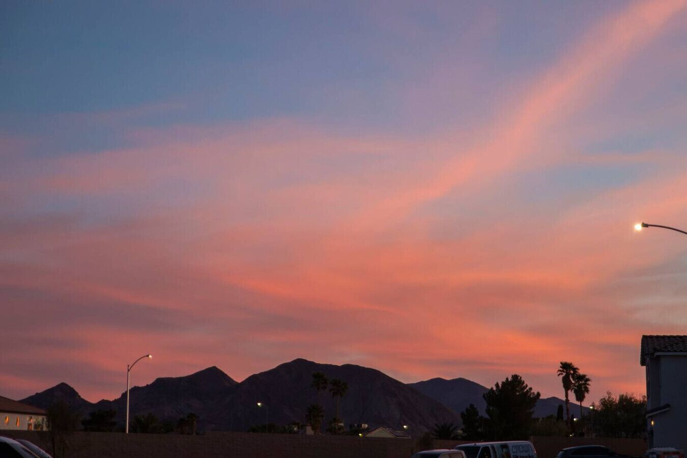 Un coucher de soleil avec des montagnes en arrière-plan, des lampadaires et un bâtiment doté d’un toit plat.