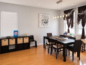 Een eetruimte met een houten tafel, stoelen, een decoratief object aan de muur en een raam met gordijnen.