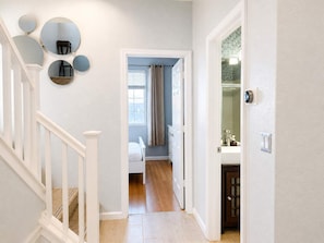 Een hal met een trap, een deur naar een slaapkamer en een badkamer met een spiegel en lichtschakelaar.