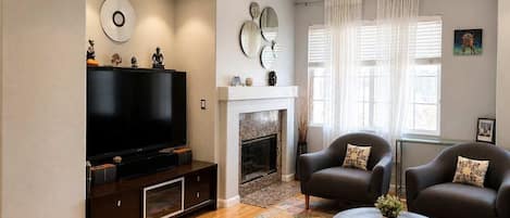 A living room with a flat-screen TV, fireplace, two armchairs, and a coffee table.