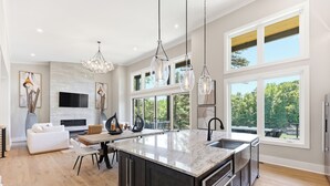Una cocina moderna con una isla grande, armarios oscuros, electrodomésticos de acero inoxidable y amplias ventanas con vistas al exterior.