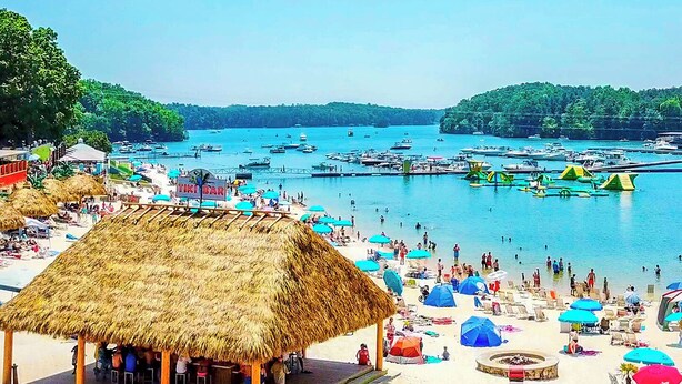 Una playa con una cabaña de techo de paja, sombrillas y barcos en el agua.