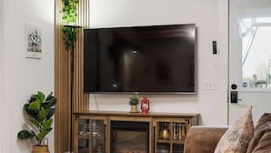 Een woonkamer met een flatscreen-tv aan de muur, een houten kast met glazen deuren, een open haard en een bank.