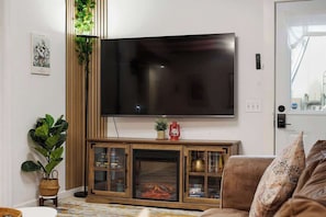 Una sala de estar con un televisor de pantalla plana montado en la pared, un mueble de madera con puertas de vidrio, una chimenea y un sofá.