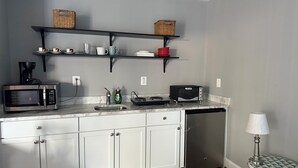 A kitchen with white cabinets, a microwave, a toaster, a sink, and a dishwasher. There are shelves above the counter holding baskets and dishes. - Cozy 1-bedroom studio in pleasant Crofton with AC (Crofton)