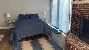 A bedroom with a bed, two bedside tables, a fireplace, and a window with curtains. - Cozy 1-bedroom studio in pleasant Crofton with AC (Crofton)
