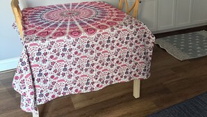 A dining table with a patterned tablecloth, a chair, and a kitchen area with shelves and appliances. - Cozy 1-bedroom studio in pleasant Crofton with AC (Crofton)