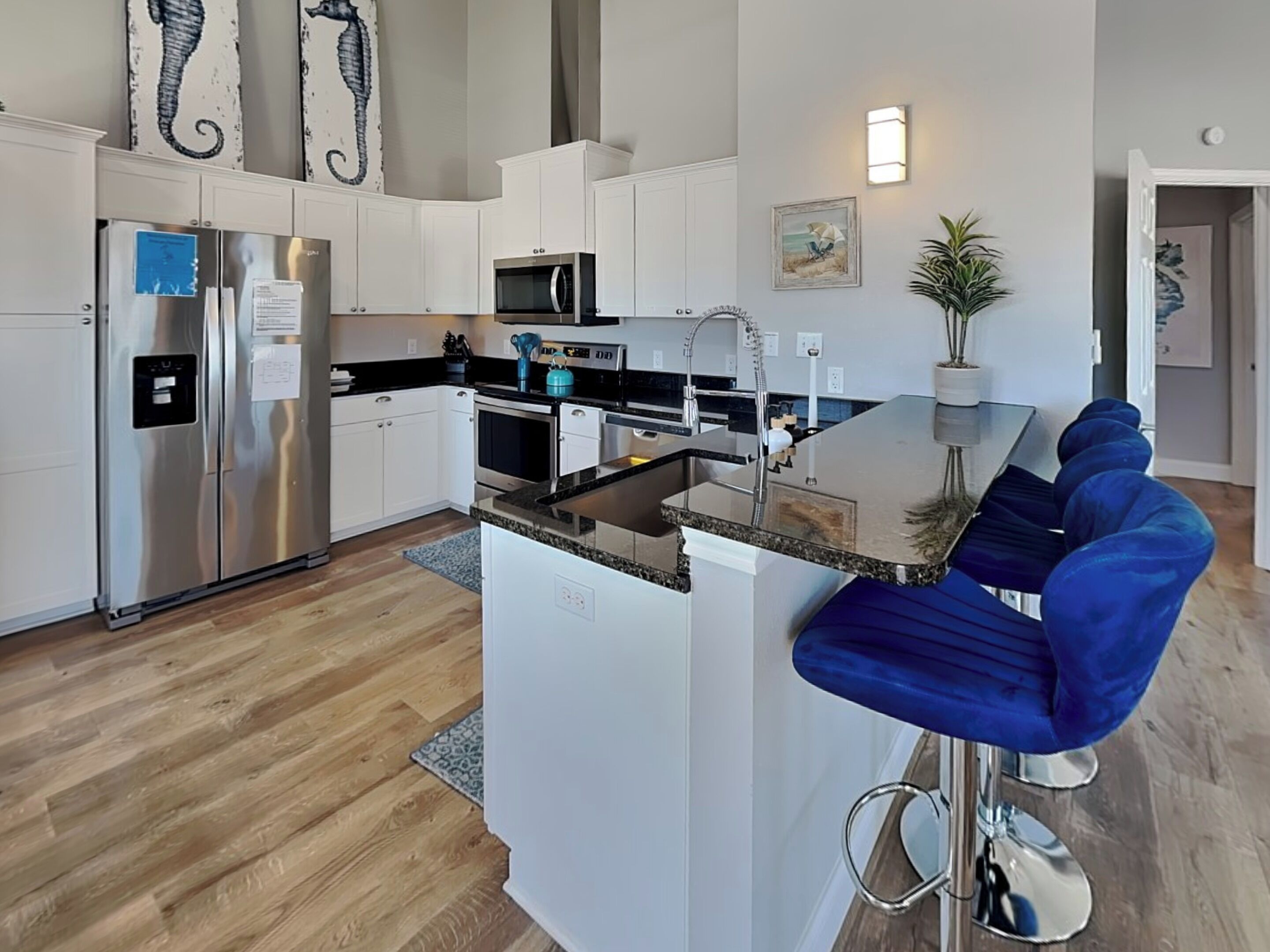 A modern kitchen with a central island, stainless steel appliances, and a seating area with blue chairs.