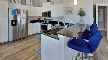 A modern kitchen with a central island, stainless steel appliances, and a seating area with blue chairs.