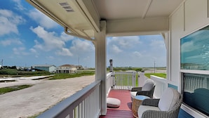 A balcony with wicker furniture, a red floor, and a view of houses and a road. - Inn at Sea La Vie (Rockport)