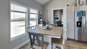 A modern kitchen with a wooden table, white chairs, a refrigerator, and a view of the outside. - Inn at Sea La Vie (Rockport)