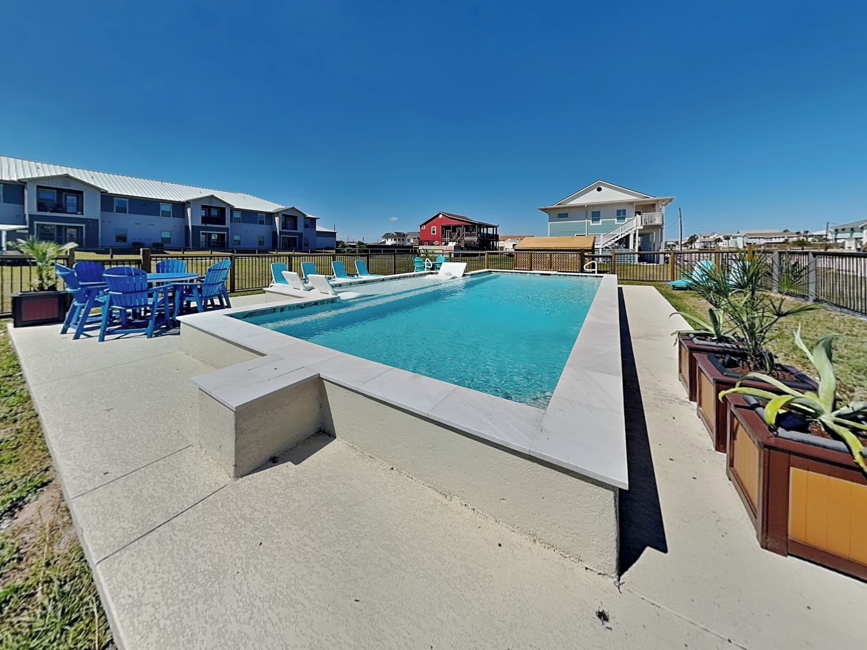 A rectangular swimming pool with a small deck area, surrounded by a fence.