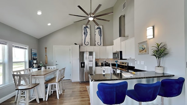 A modern kitchen with a central island, bar stools, and a dining area with white chairs. - Inn at Sea La Vie (Rockport)