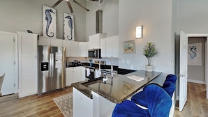 A modern kitchen with white cabinetry, stainless steel appliances, and a central island with blue bar stools. - Inn at Sea La Vie (Rockport)