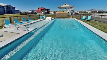 A rectangular swimming pool with clear blue water, surrounded by a wooden deck and multiple lounge chairs.