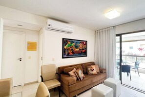Ein Wohnzimmer mit einem braunen Sofa, einem Sessel, einem Gemälde, einer Klimaanlage und einer Glasschiebetür nach draußen.