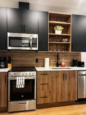 Eine moderne Küche mit Edelstahl-Mikrowelle, Backofen und Geschirrspüler, Holzschränken und einem Holzregal mit Gläsern.