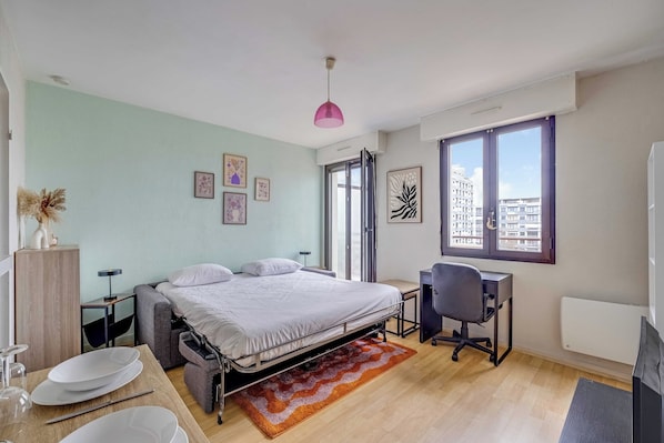 A bedroom with a bed, desk, chair, and large windows. - Spacious Studio 2P - Near La Defense (Courbevoie)